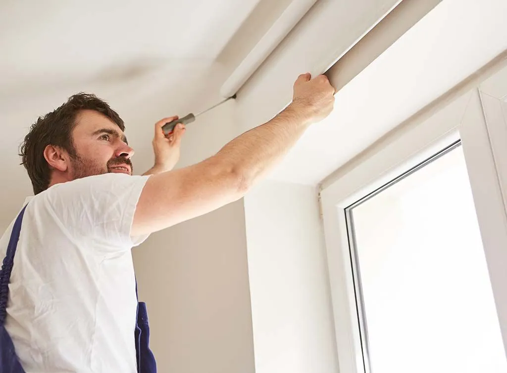 Technician using a tool to repair or install a roller blind on a window frame indoors