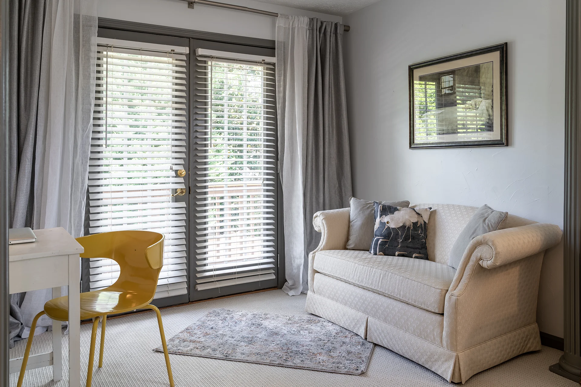 Bright cozy living room interior featuring white window blinds on glass doors, a white sofa, and a yellow chair