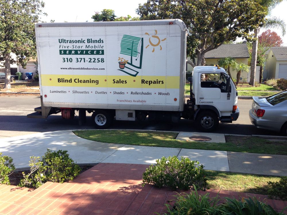 A white mobile service truck parked on a residential street for Ultrasonic Blinds Services